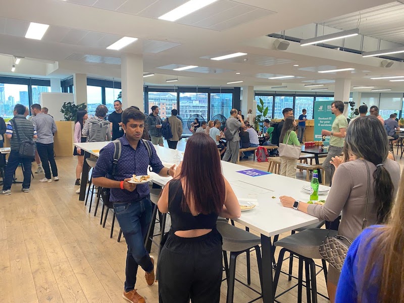 The kitchen in the Deliveroo offices filled with several groups of people chatting over food and drink