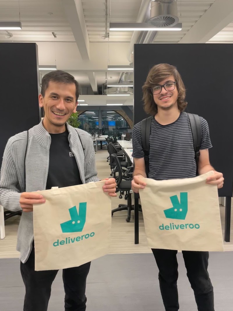 Two attendees showing off their free Deliveroo branded tote bags, smilling at the camera